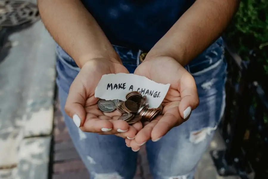 Hands holding coins and a note reading Make a change, representing direct financial support for community impact.
